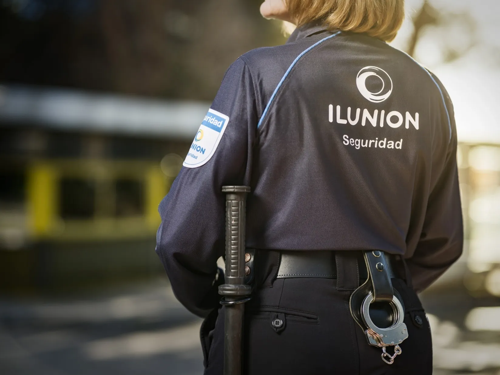 Profesional de la Seguridad de Ilunion mostrando el logo corporativo de Ilunion Seguridad en la espalda de su uniforme