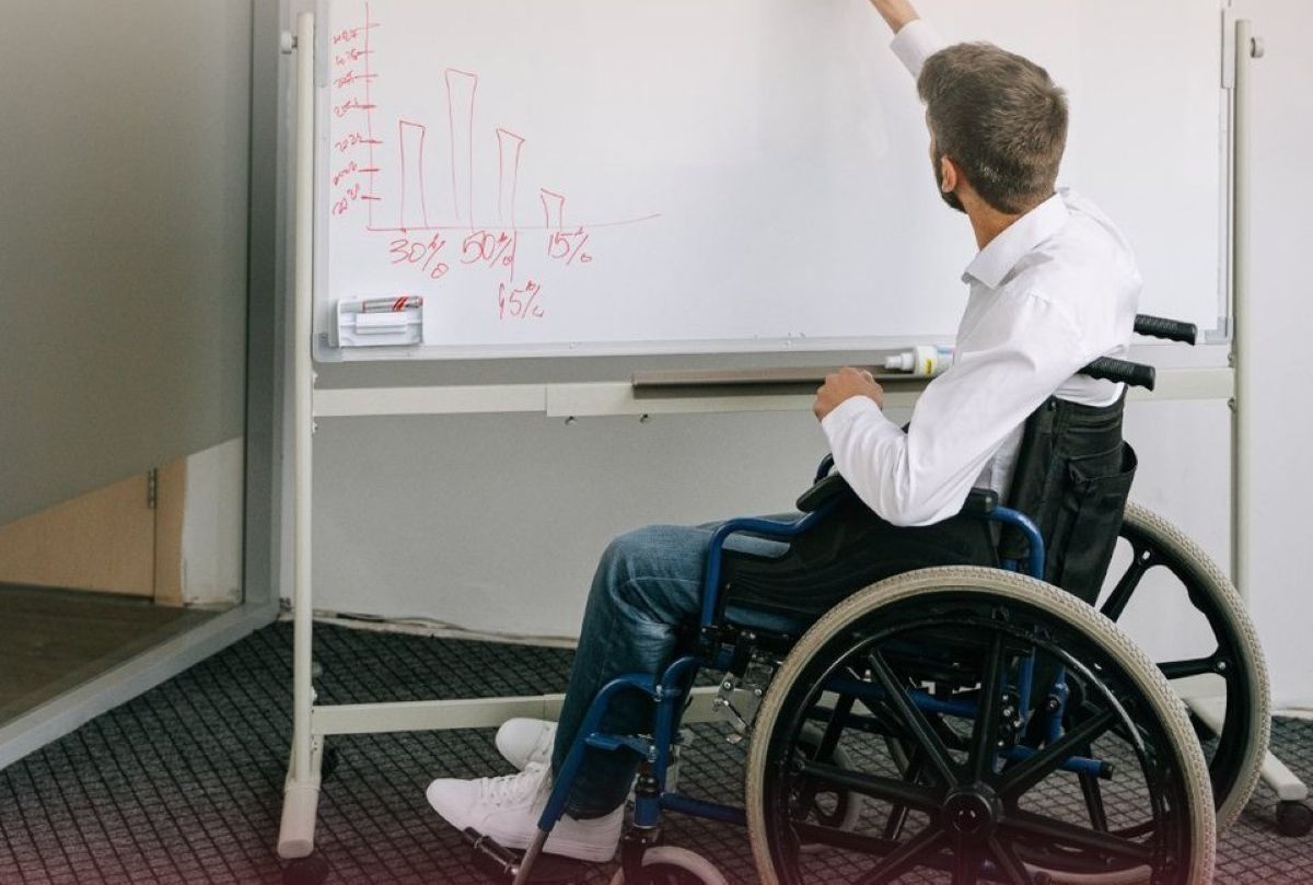 Joven en silla de ruedas frente a una pizarra realizando un gráfico