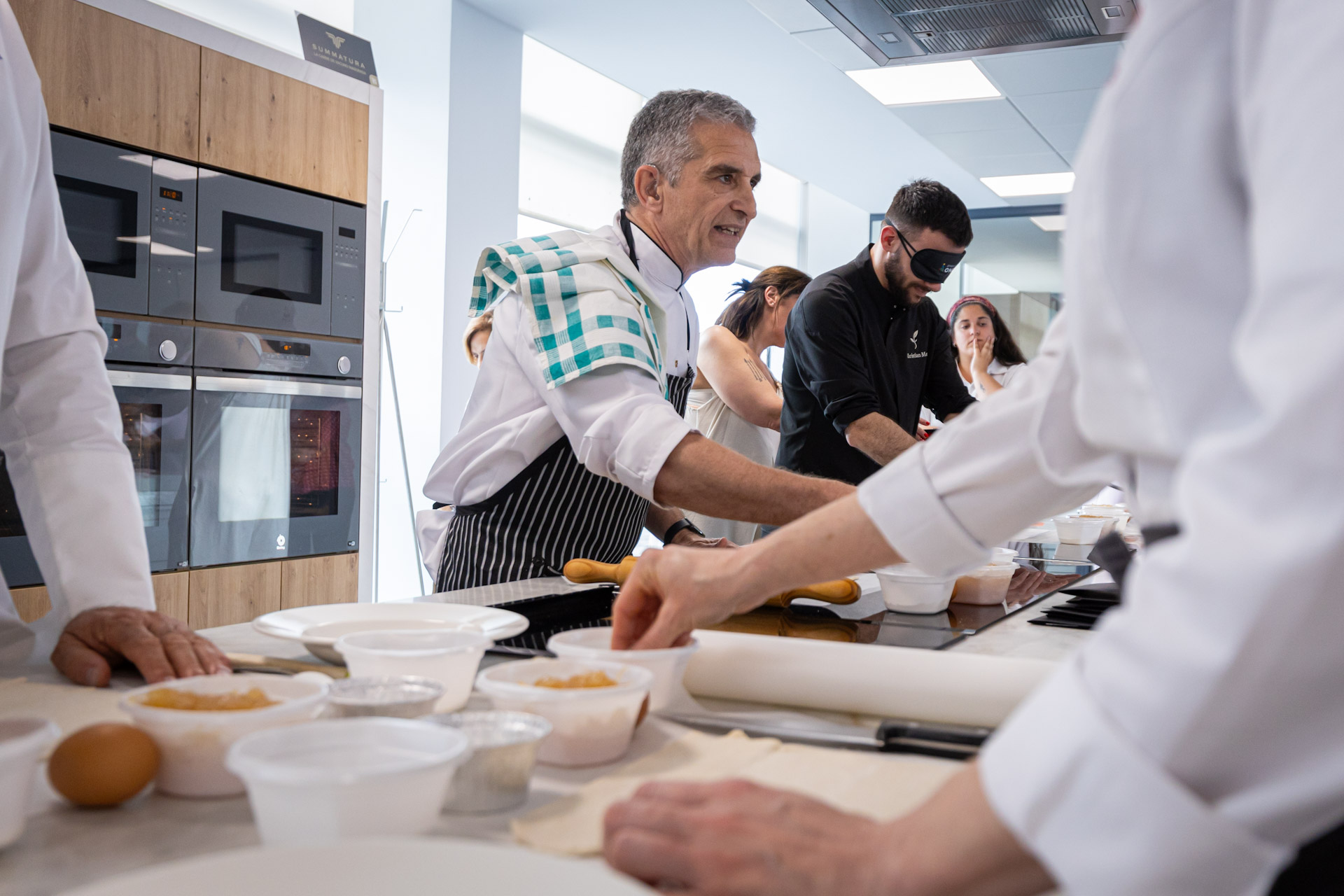 Rafael Zapata realizando la receta, seguida por los cocineros profesionales provistos de antifaz