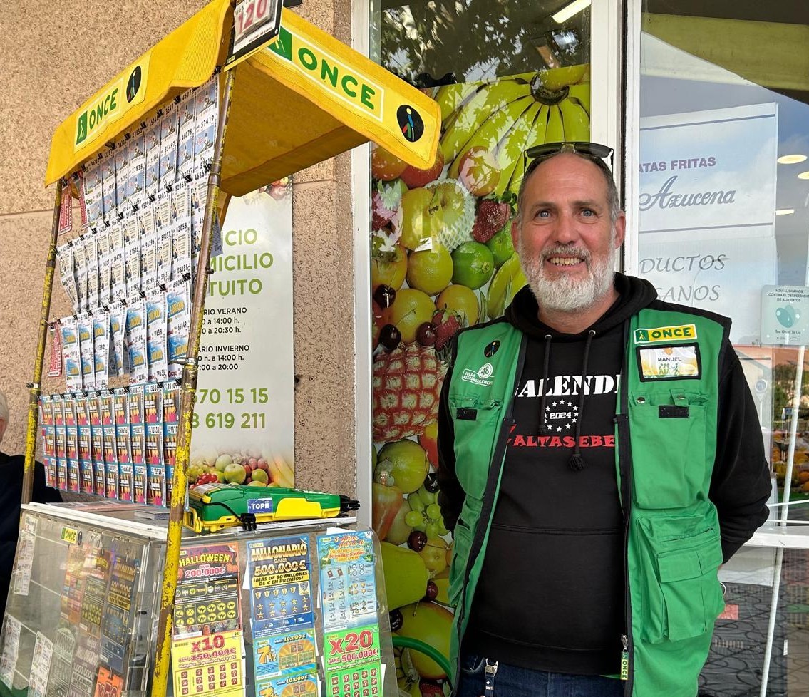 Manuel Brea Portero, vendedor de los productos de lotería de la ONCE, posa sonriente junto a su expositor de venta en Rivas Vaciamadrid