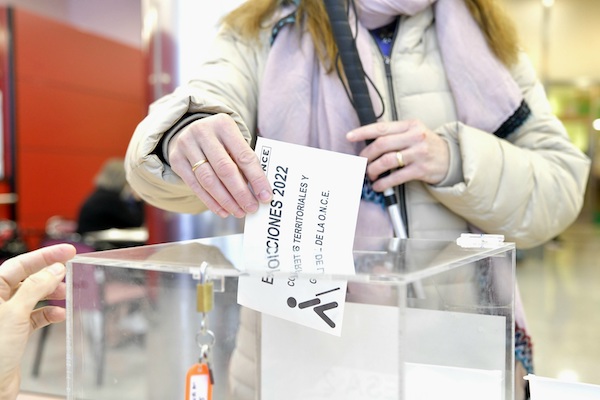 Las manos de una chica joven echando una papeleta de votación a una urna transparente.
