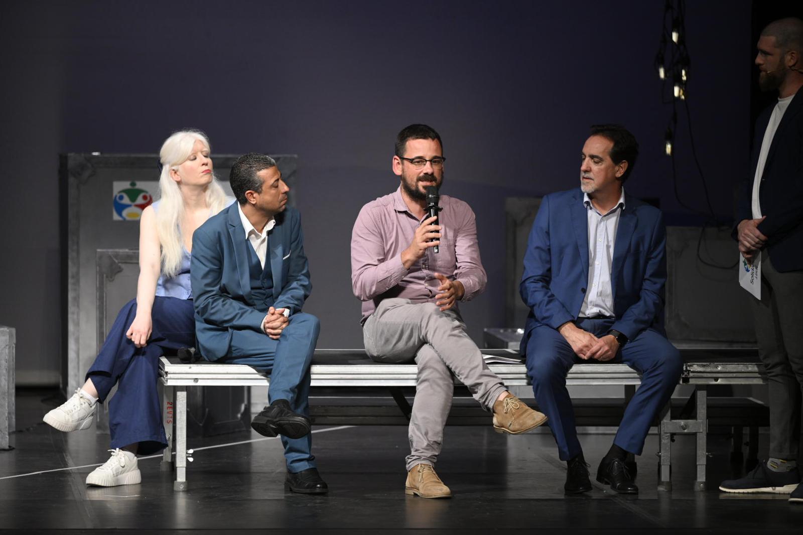 Los presentadores charlando, con un micrófono de mano, sentados en una plataforma, junto a autoridades ONCE