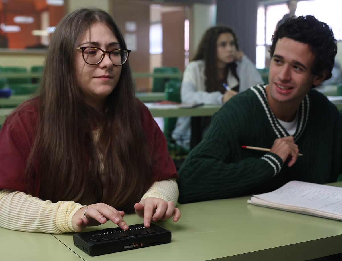 Un chico y una chica en clase. La chica es ciega y está escribiendo en una línea braille