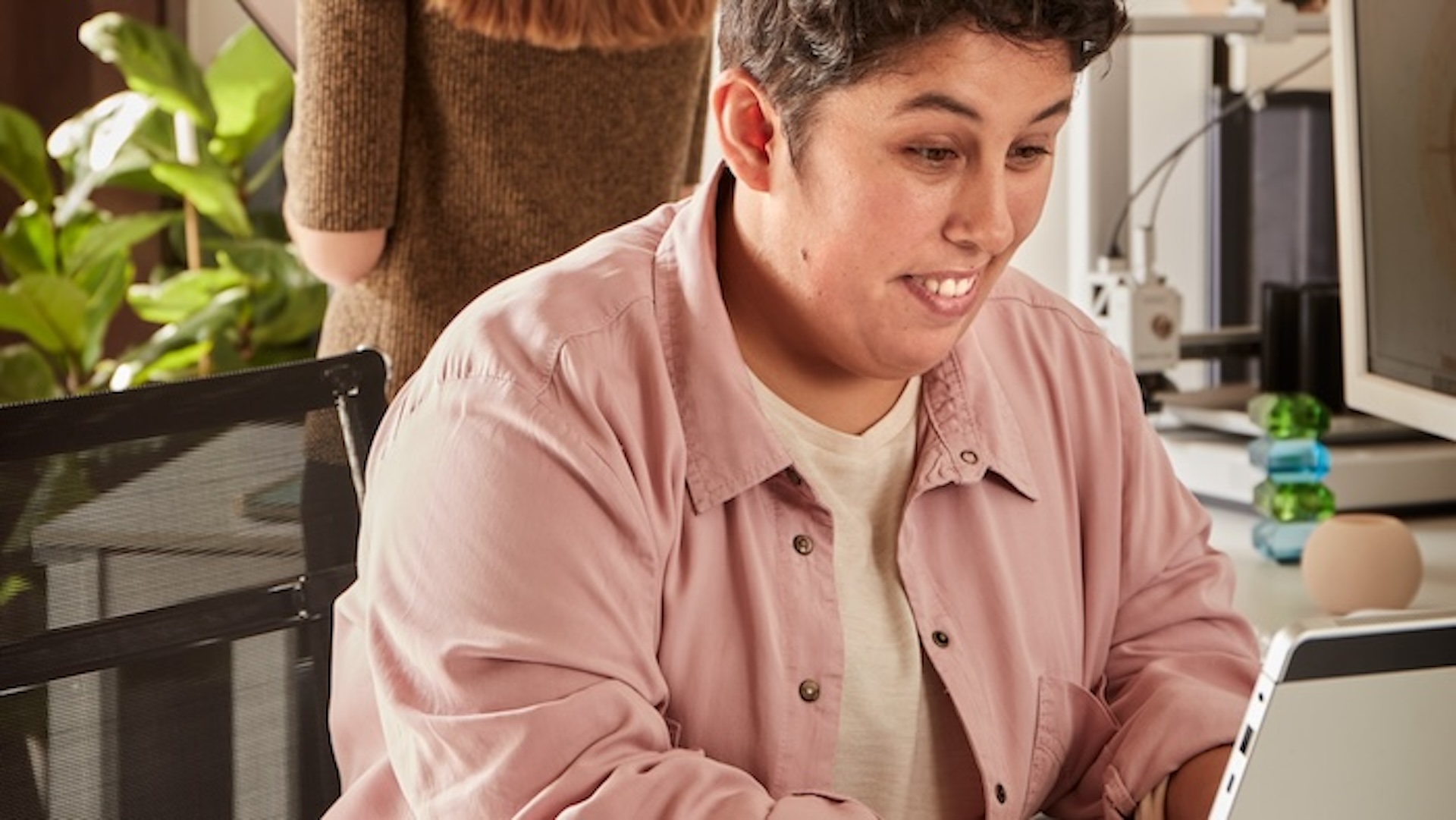 Una chica con discapacidad intelectual sonriente, trabajando en una oficina delante de un ordenador portátil