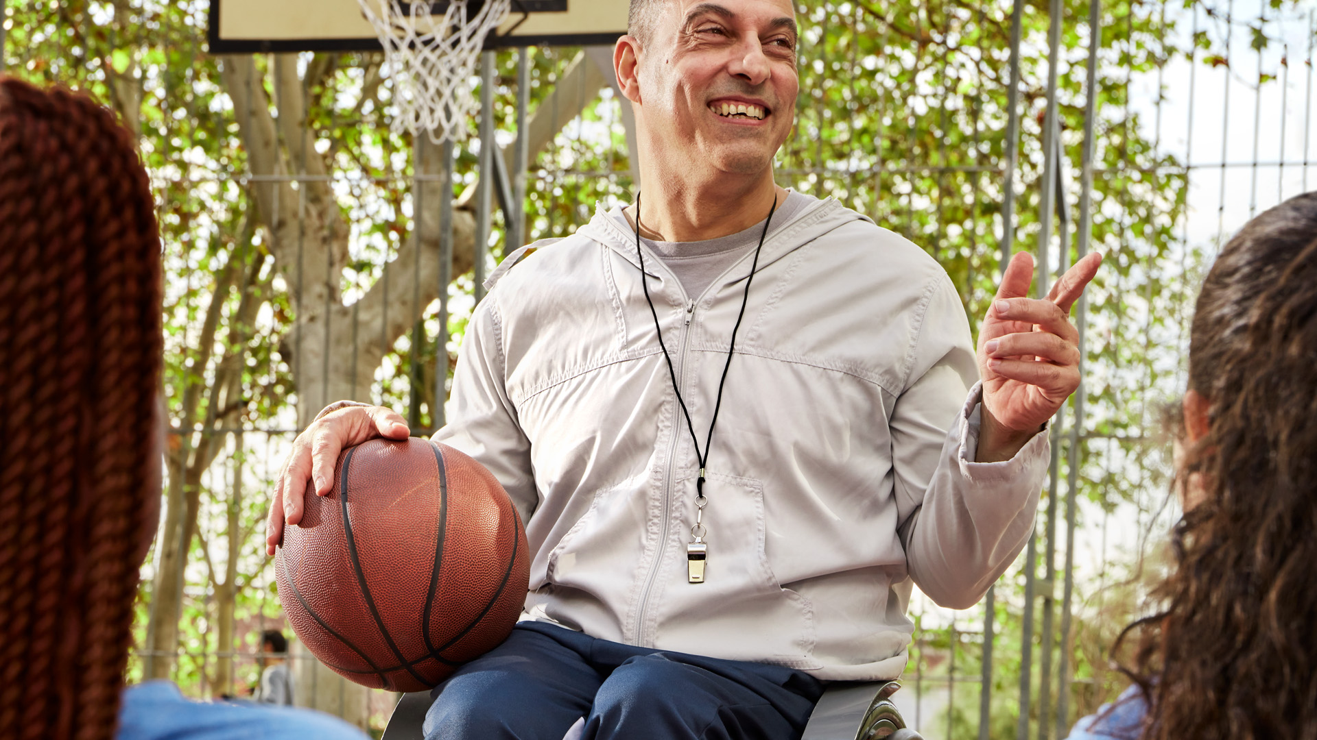 Un jugador de baloncesto en silla de ruedas con un balón en las manos, en el parque, al fondo árboles