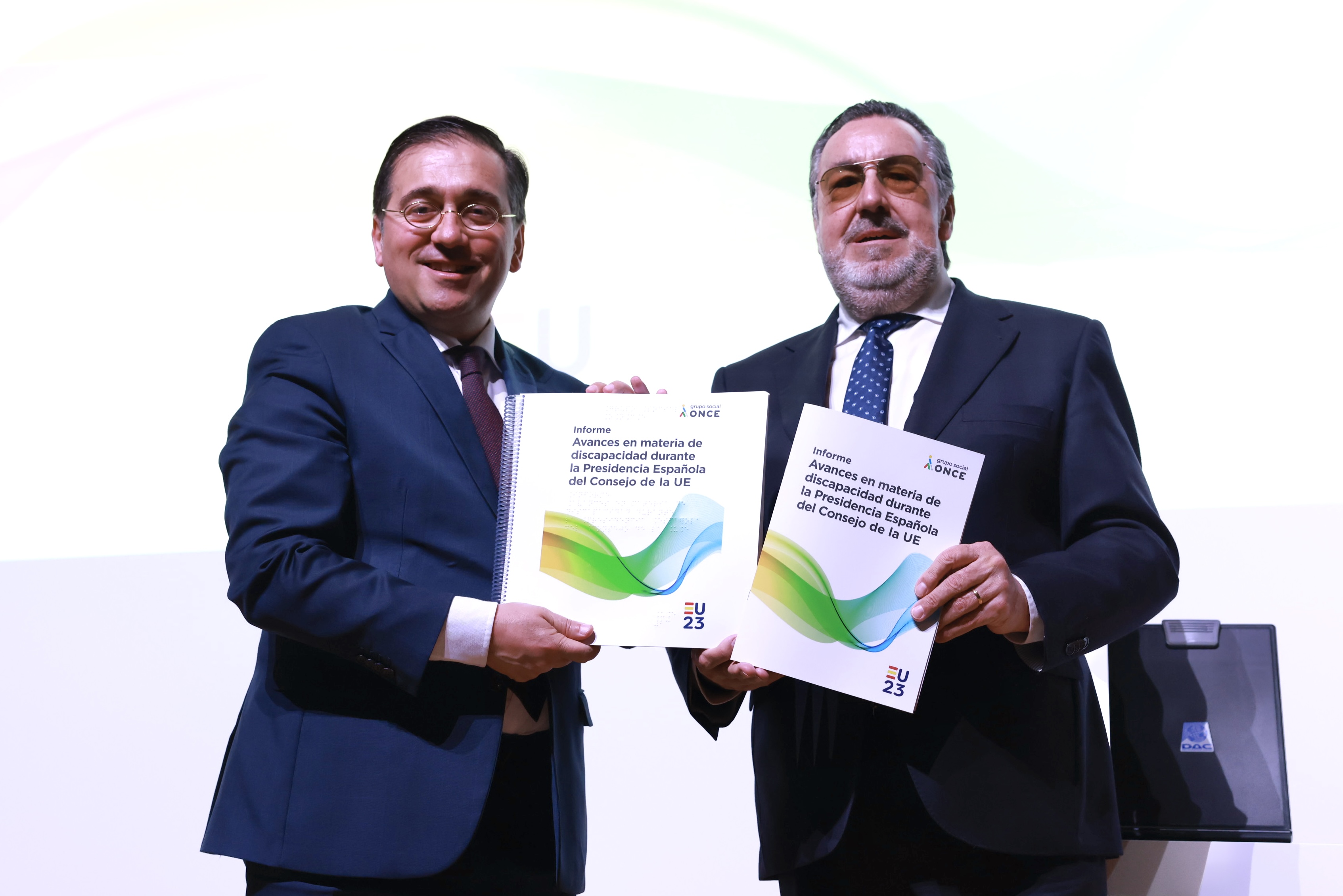 Primer plano de José Manuel Albares y Miguel Carballeda sujetando los informes sobre el escenario