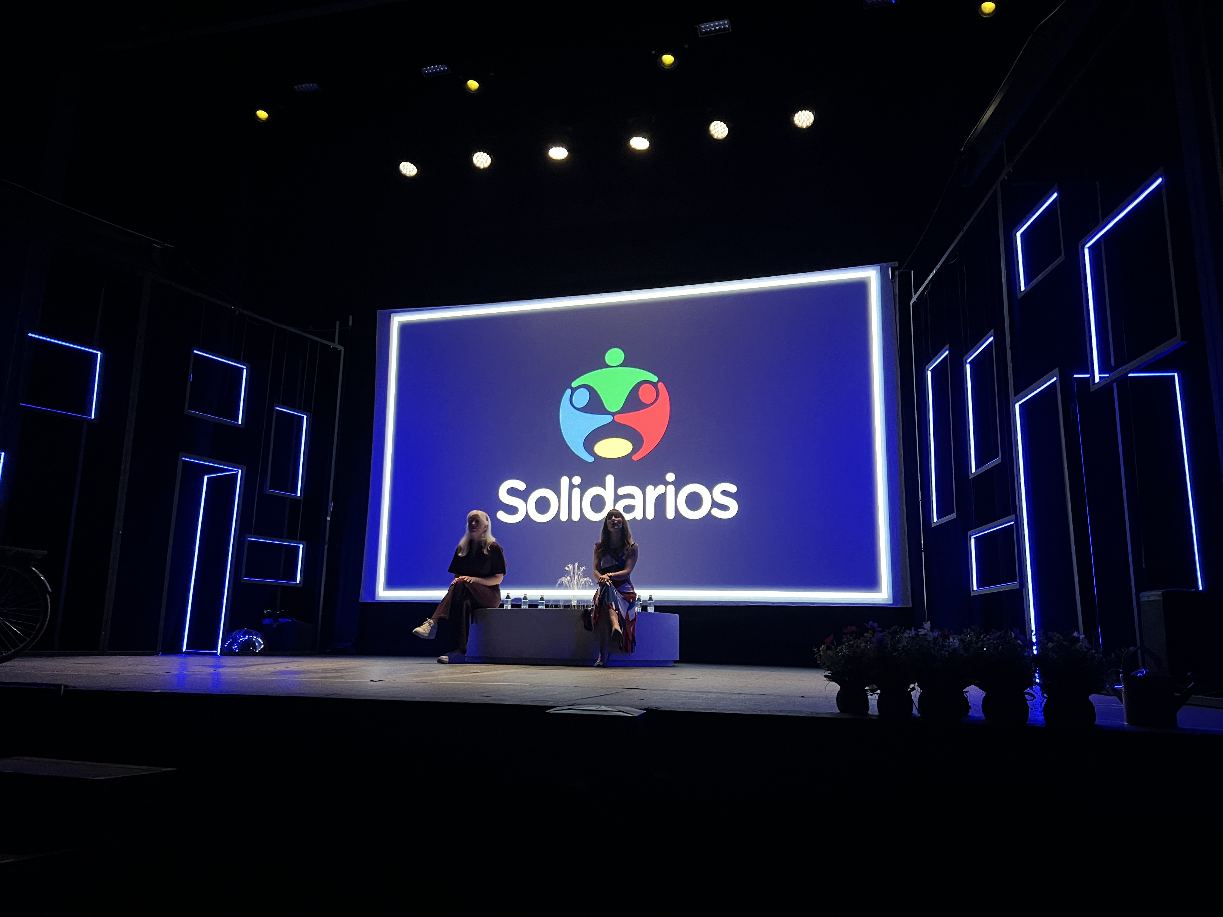 Imagen de una gala de los Premios Solidarios Grupo Social ONCE con Patty Bonet y Laura Ferrer en el escenario. En la pantalla se ve el logo de los Premios Solidarios.