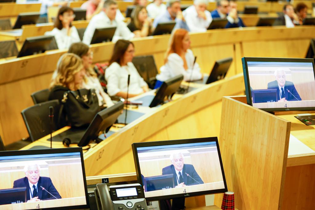 Detalle de un hombre hablando en la eurocámara semicircular retransmitido en diferentes pantallas de ordenador portátil