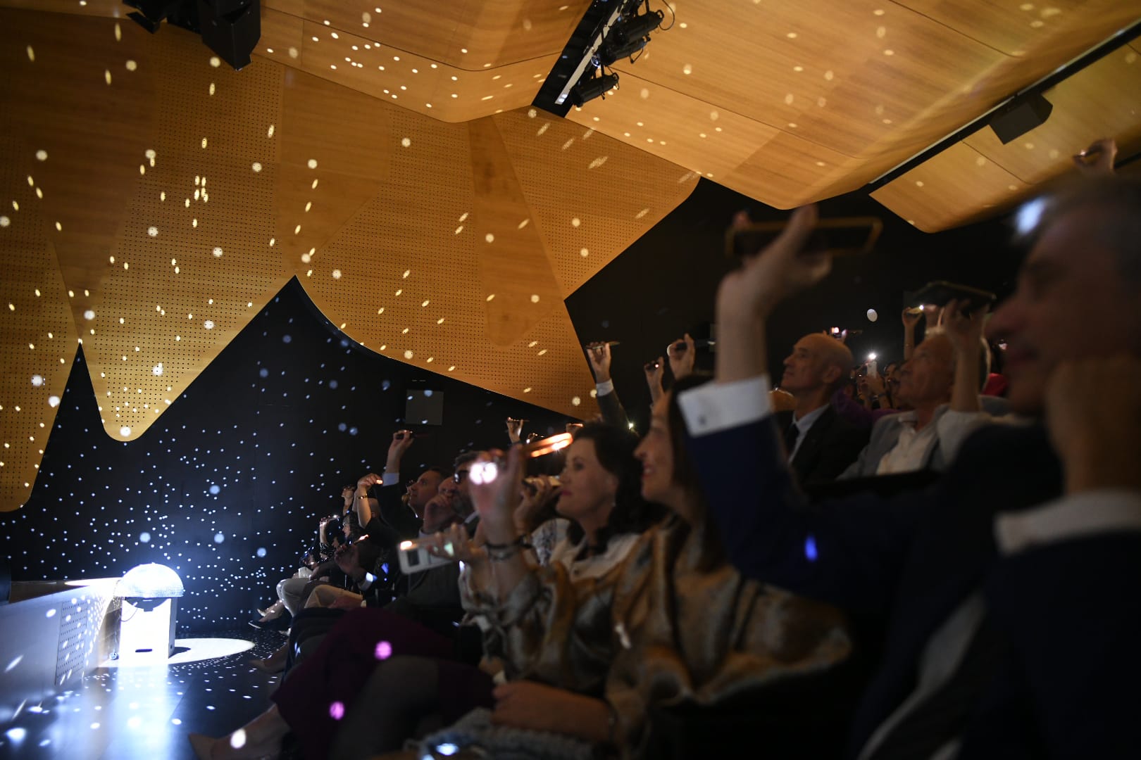 Asistentes a la gala de los Premios Solidarios del Grupo Social ONCE Aragón con las linternas de sus móviles iluminando el palco de butacas junto a la iluminación de la escena