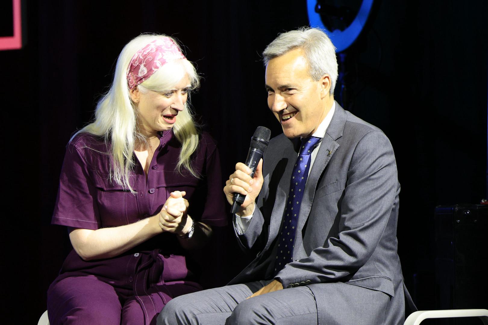 Patty Bonet, presentadora, y Alejandro Oñoro, consejero ONCE e Ilunion, hablando sentados en la fuente del escenario