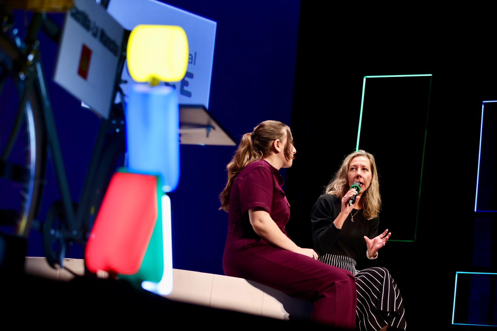 Oncelio de colores en primer plano y detrás escenario con dos mujeres sentadas hablando