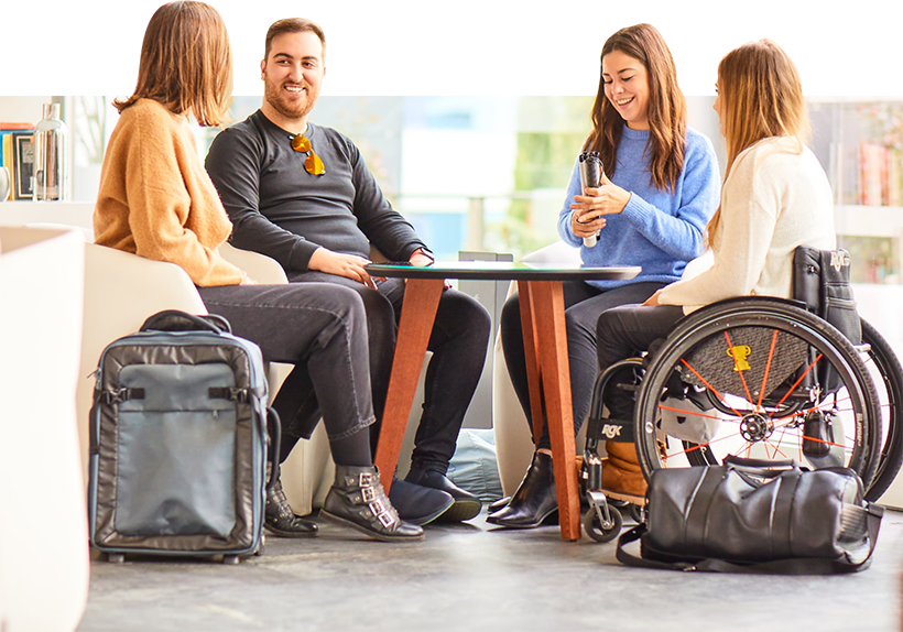 Grupo de cuatro personas sentadas y hablando. Una de ellas está plegando un bastón blanco y otra está sentada en una silla de ruedas