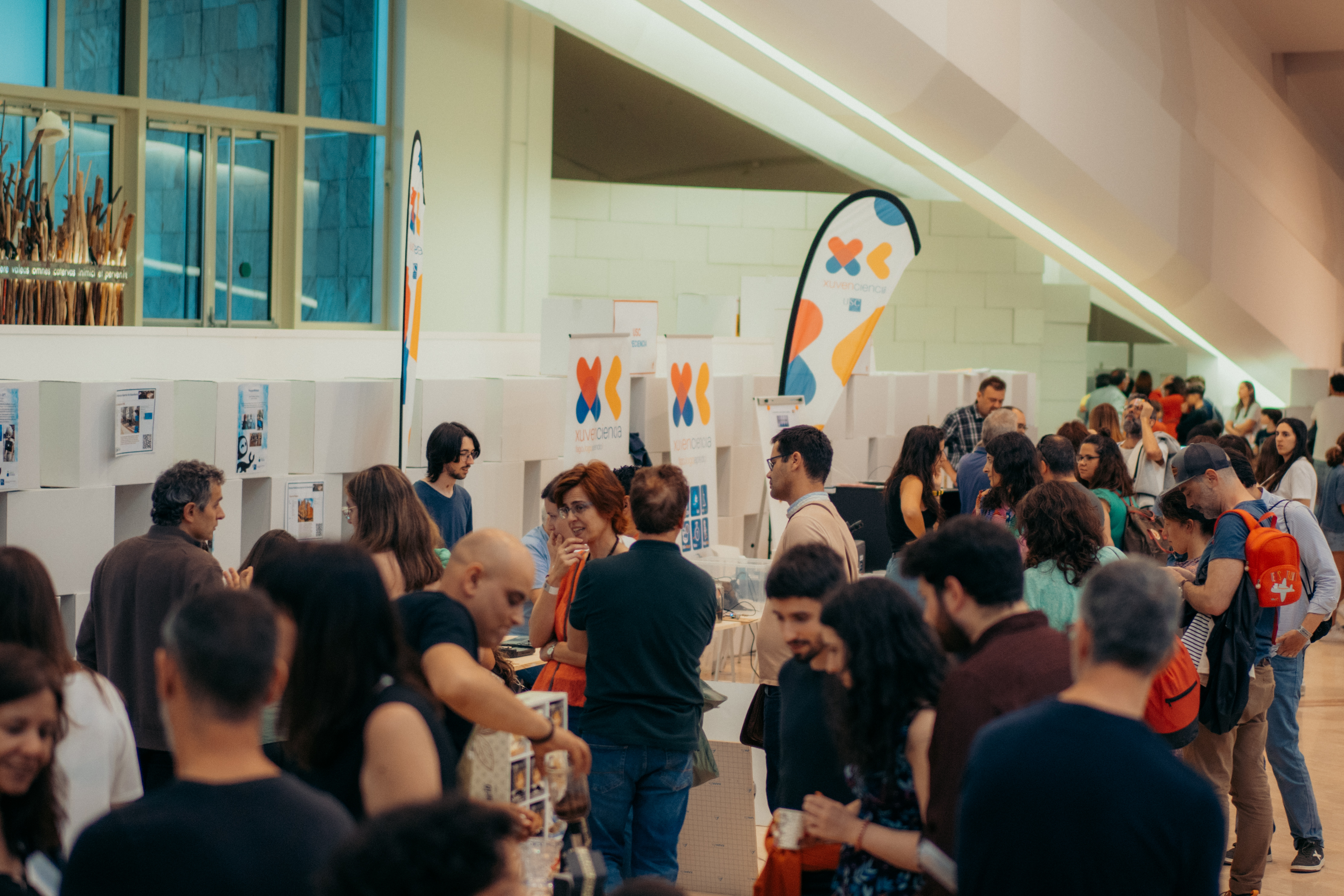 Vistazo de uno de los pasillos de la Maker Faire Galicia con gente consultando los distintos stands y banderas