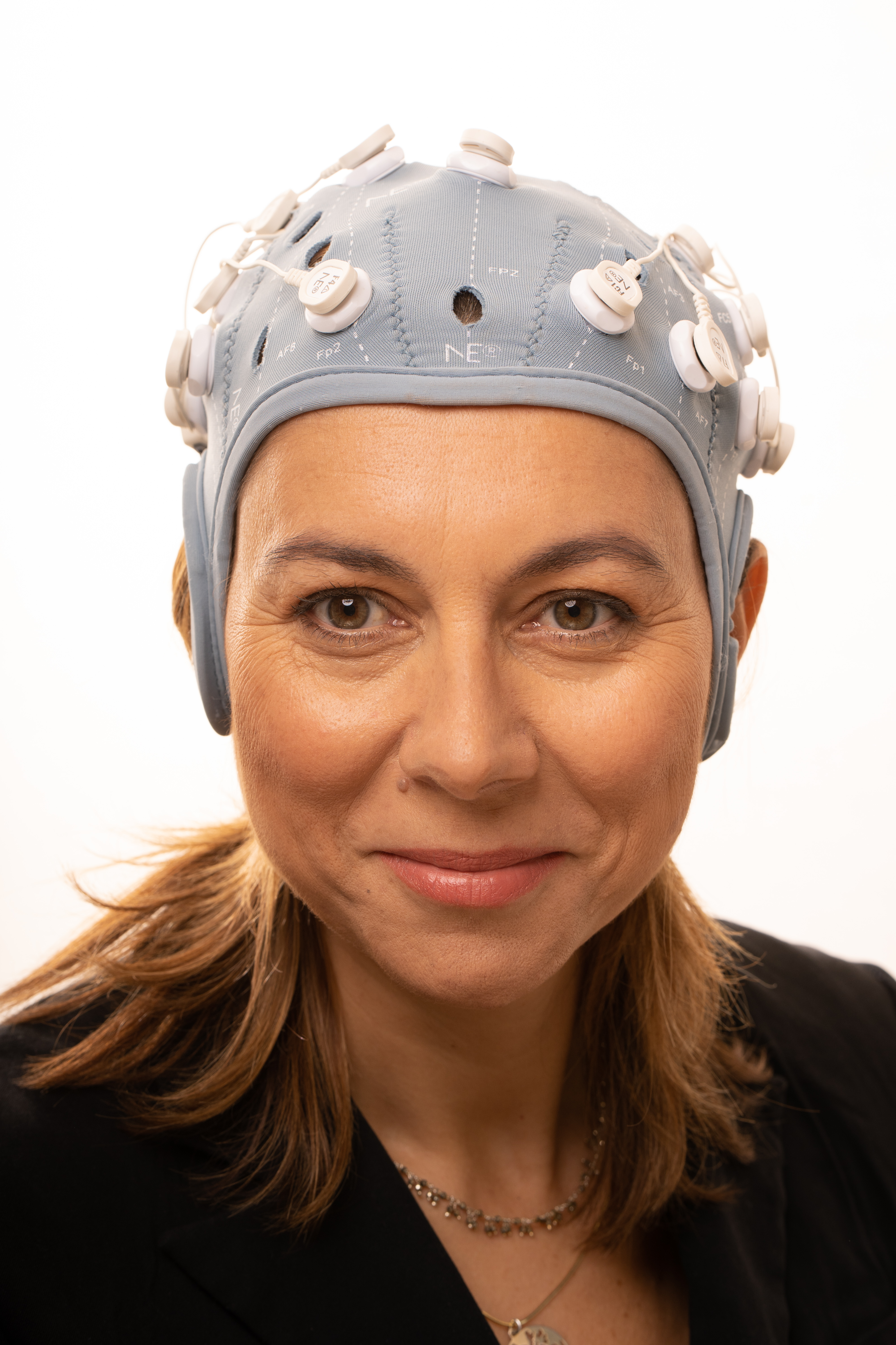 Ana Maiques en primer plano, mirando directamente a cámara con una expresión tranquila y segura. Lleva puesto un dispositivo tipo gorro ajustado de color gris claro, equipado con varios sensores distribuidos por toda la superficie, conectados mediante pequeños cables.