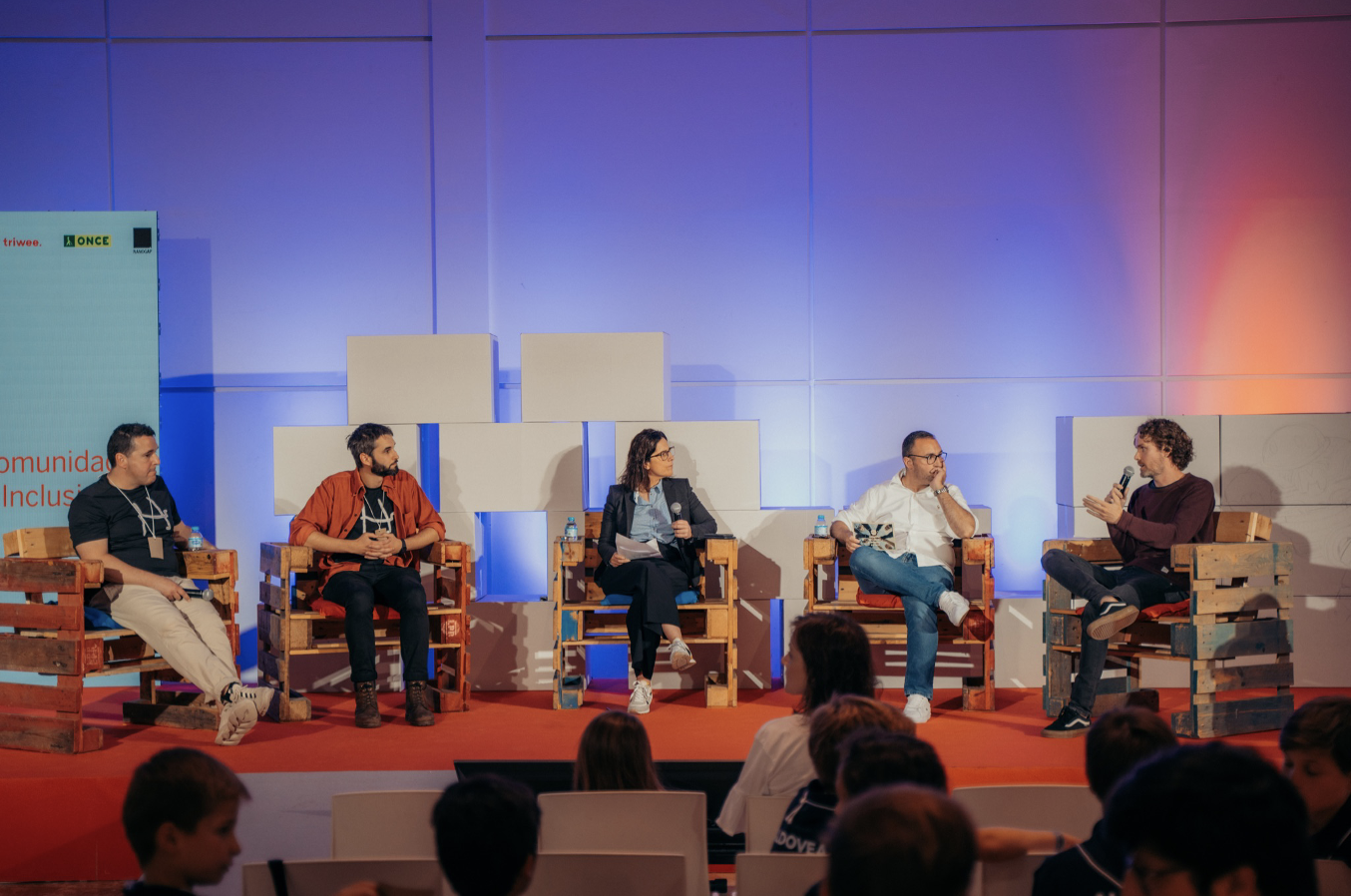 Mesa redonda con participantes sentados en sillones y cartelería de la Maker Faire