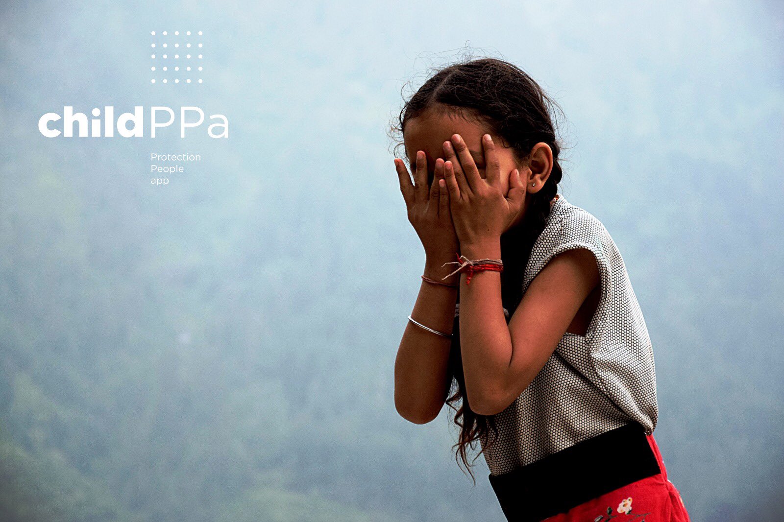 Niña india, pequeña, de unos 7 años con trenzas y con las dos manos tapándose la cara. Lleva varias pulseras en las muñecas y está en una zona rural muy frondosa en una montaña de la India. En un lateral de la imagen de lee: CHILD PPA: Protection People App