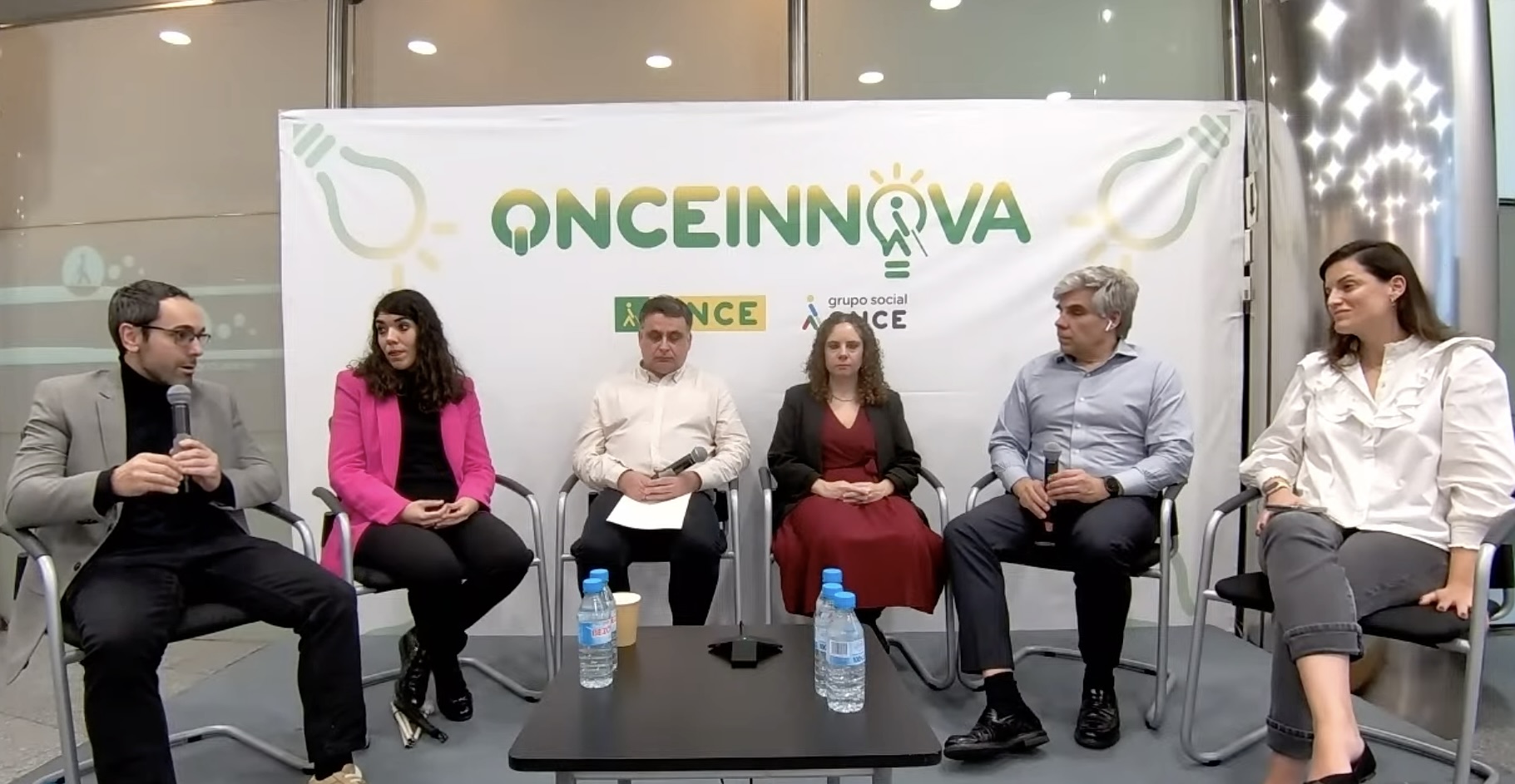 Cuatro ponentes y el presentador y la presentadora del Jueves de ONCE Innova de Enero, sentados en el escenario desde donde se retransmitió el evento en la Delegación de Madrid de ONCE. De izquierda a derecha están con el micro, Jesús Sánchez del CRE de Madrid, a su lado Tatiana Moreiro de la  Escuela Universitaria de Fisioterapia ONCE, sigue también con micro en la mano José Rodríguez, Jefe de Coordinación de la Imprenta Cupón ONCE, la su lado está Mª José Torrado, Jefa de Coordinación en la Delegación Territorial de Madrid y finalizando están Cristian Sainz (con micro en mano)y Ana Ortega del equipo de ONCE Innova. Detrás de todos ellos está la imagen en grande de ONCE Innova. 