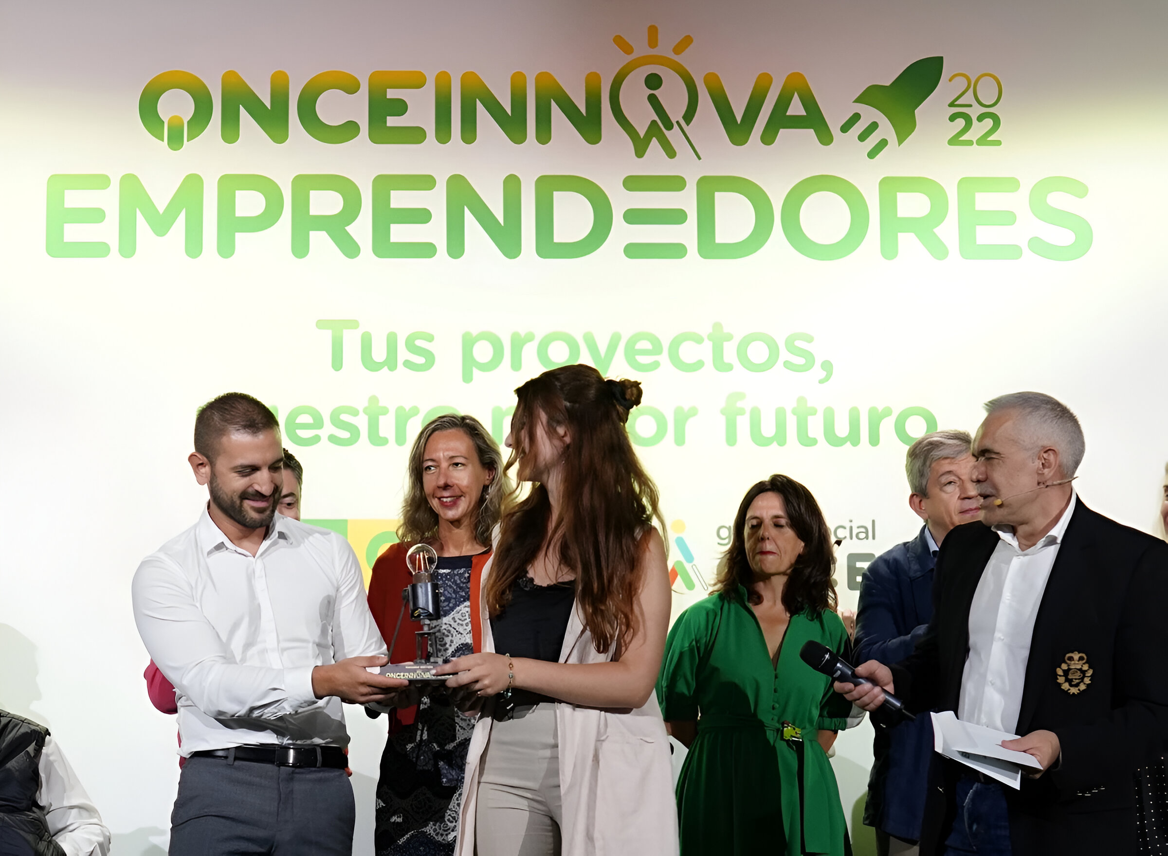 Imagen de la final del RETO ONCE Innova Emprendedores 2022. Hay un grupo de personas en el escenario entregando el premio a dos de los miembros de Mentiness. De Fondo sale una cartela donde sale el logo del Reto emprendedores