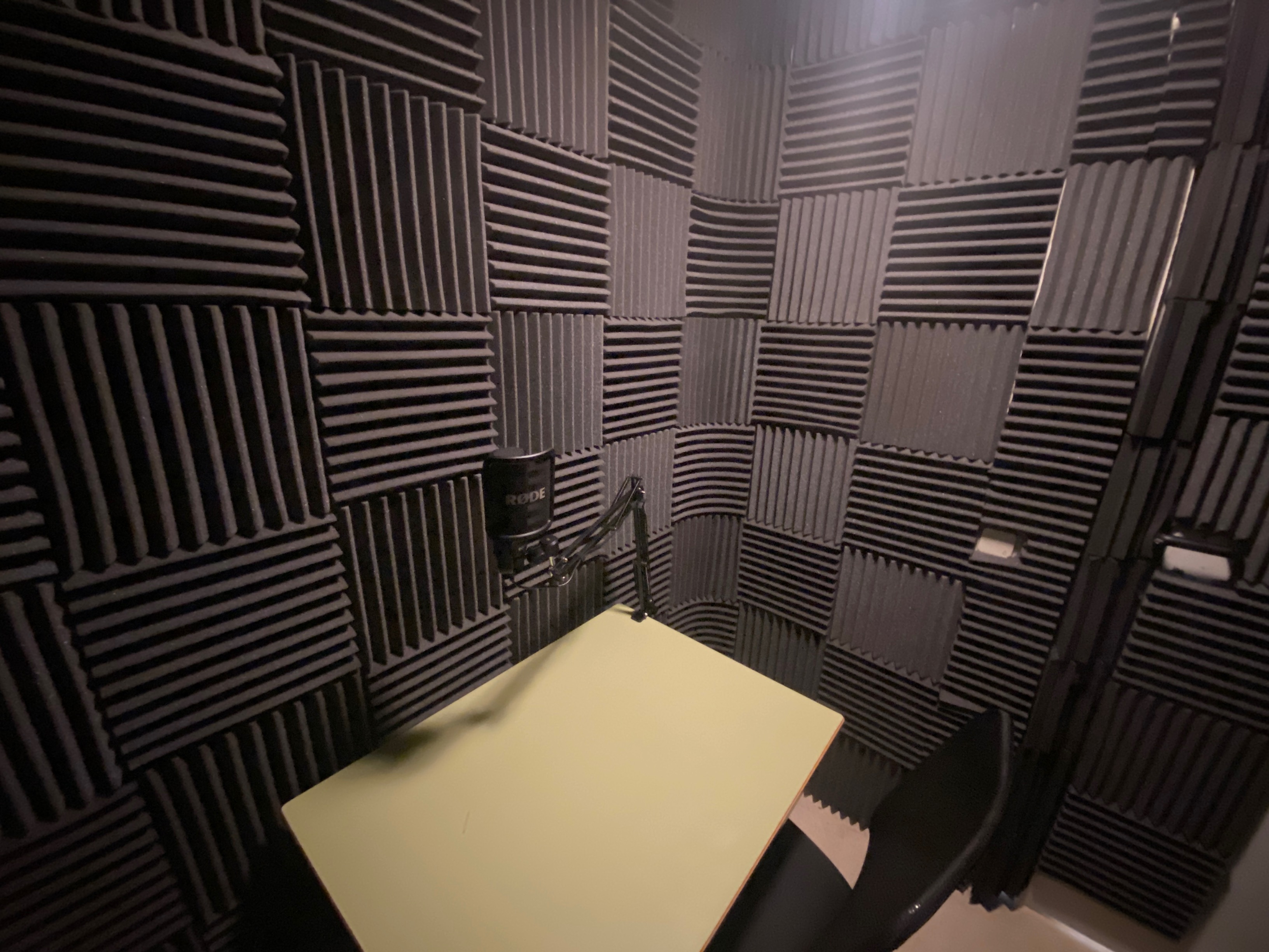 Sala de grabación de los podcast. Mesa y silla con micro en una sala con revestimiento de paneles acústicos negros.