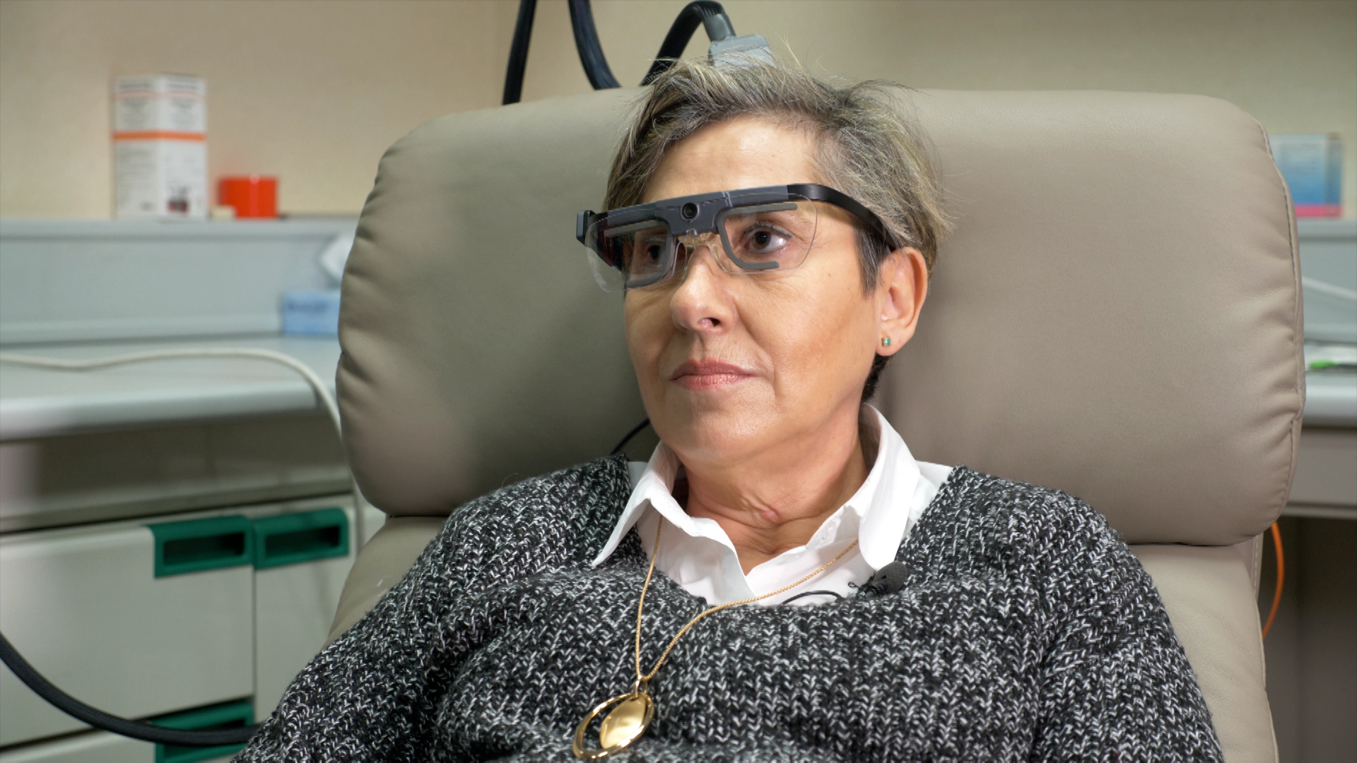 Mujer sentada en un sillón de hospital con gafas convencionales conectadas a una retina artificial. 