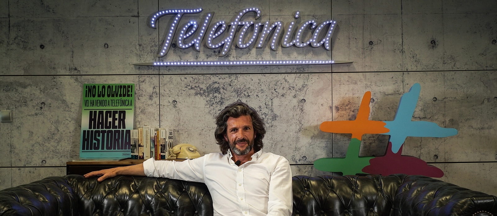 Pedro Serrahima sentado en un sofá delante de un gran letrero que pone Telefónica