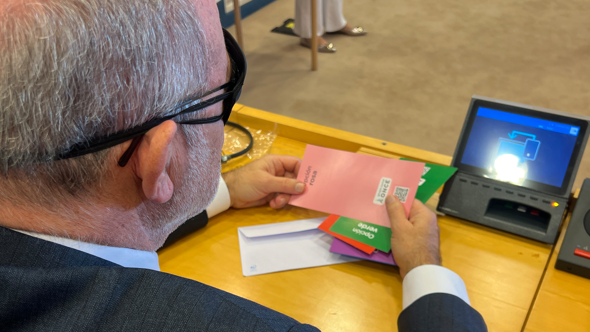 Eurodiputado escogiendo una papeleta rosa con el cógido QR con el antifaz puesto