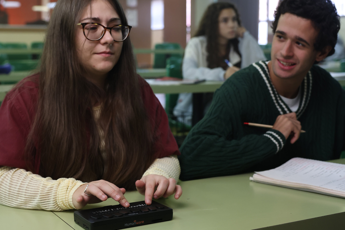 Un alumno hablando con su compañera, que es una alumna ciega utilizando una línea braille