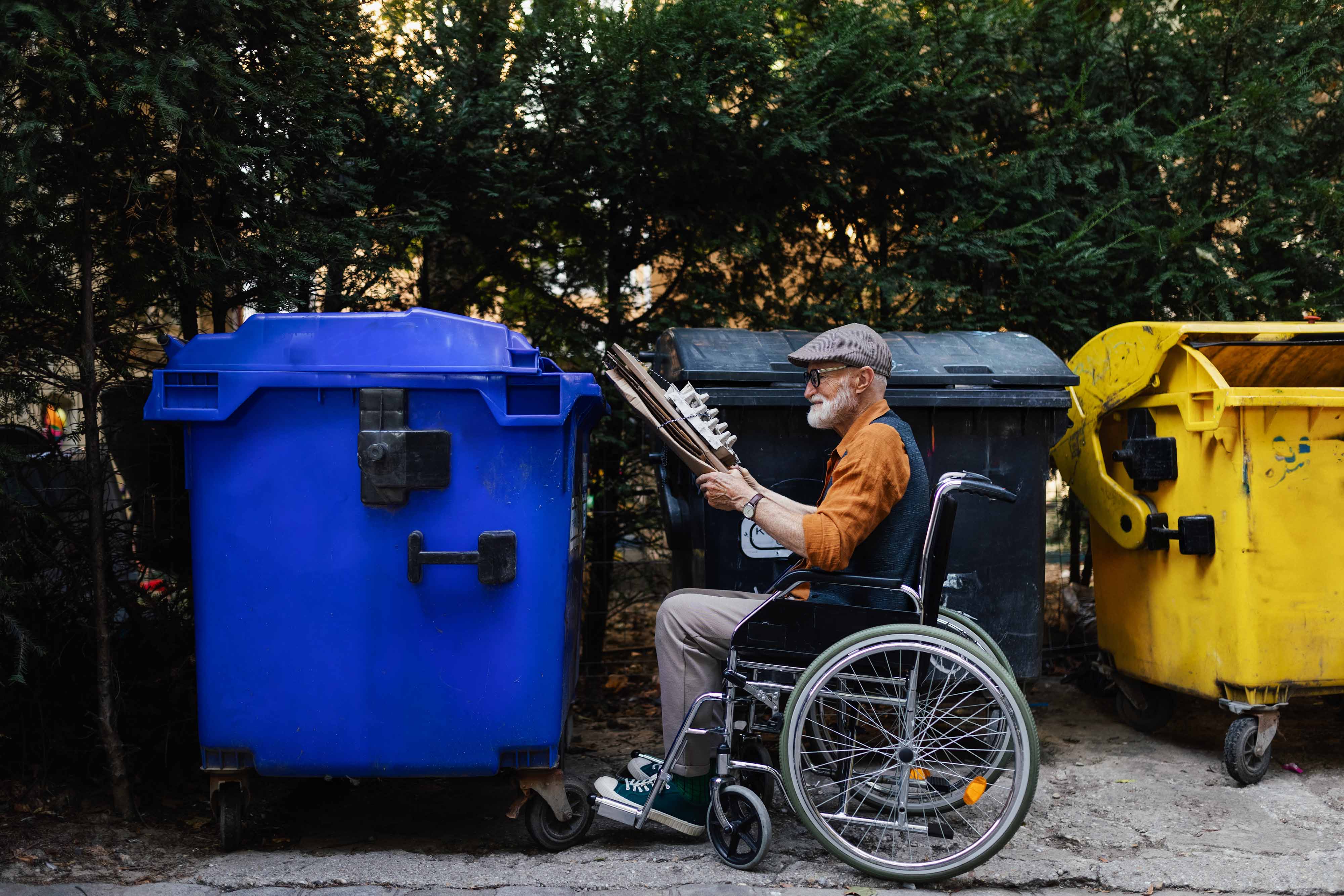 Persona mayor en silla de ruedas depositando residuos en un contenedor de reciclaje