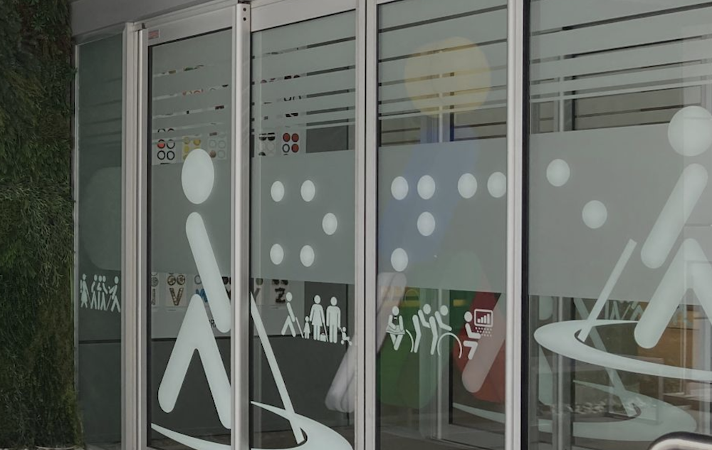 Puerta de cristal automática de un centro ONCE con Oncelio en distintas posiciones vinilado en el cristal