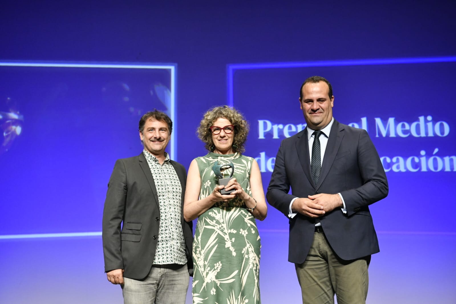 Premiados al Medio de comunicación, sonrientes sobre el escenario y con fondo azul