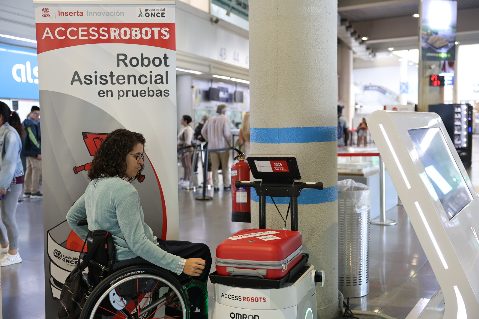 Usuaria de silla de ruedas utilizando un robot accesrobot en una terminal de autobuses