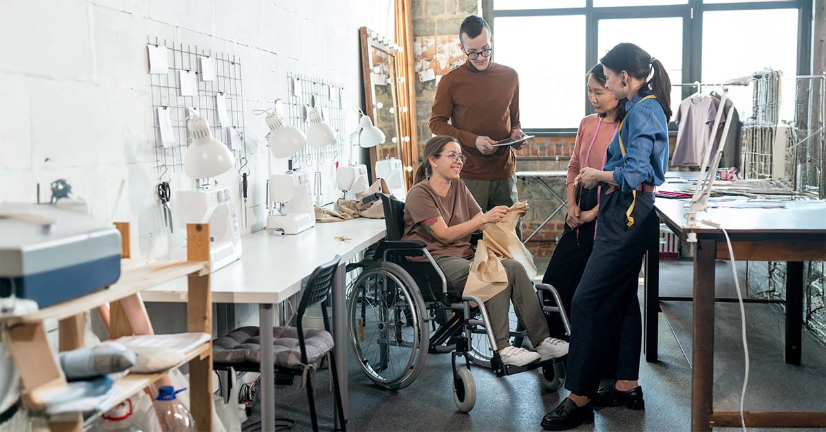 Trabajadora con discapacidad en silla de ruedas en su centro de trabajo junto a sus compañeros y compañeras