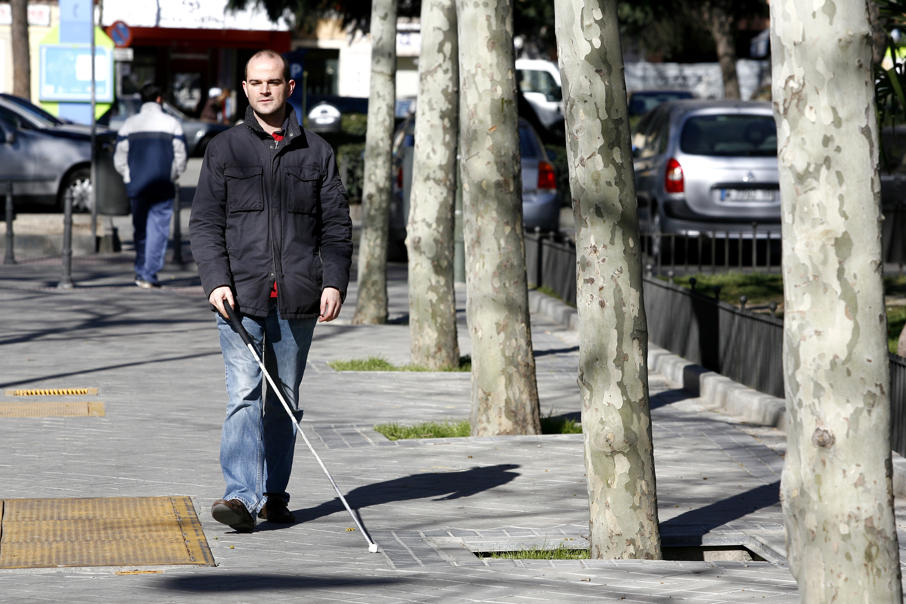 Una persona ciega deambula por la calle ayudado de un bastón blanco Una persona ciega deambula por la calle ayudado de un bastón blanco