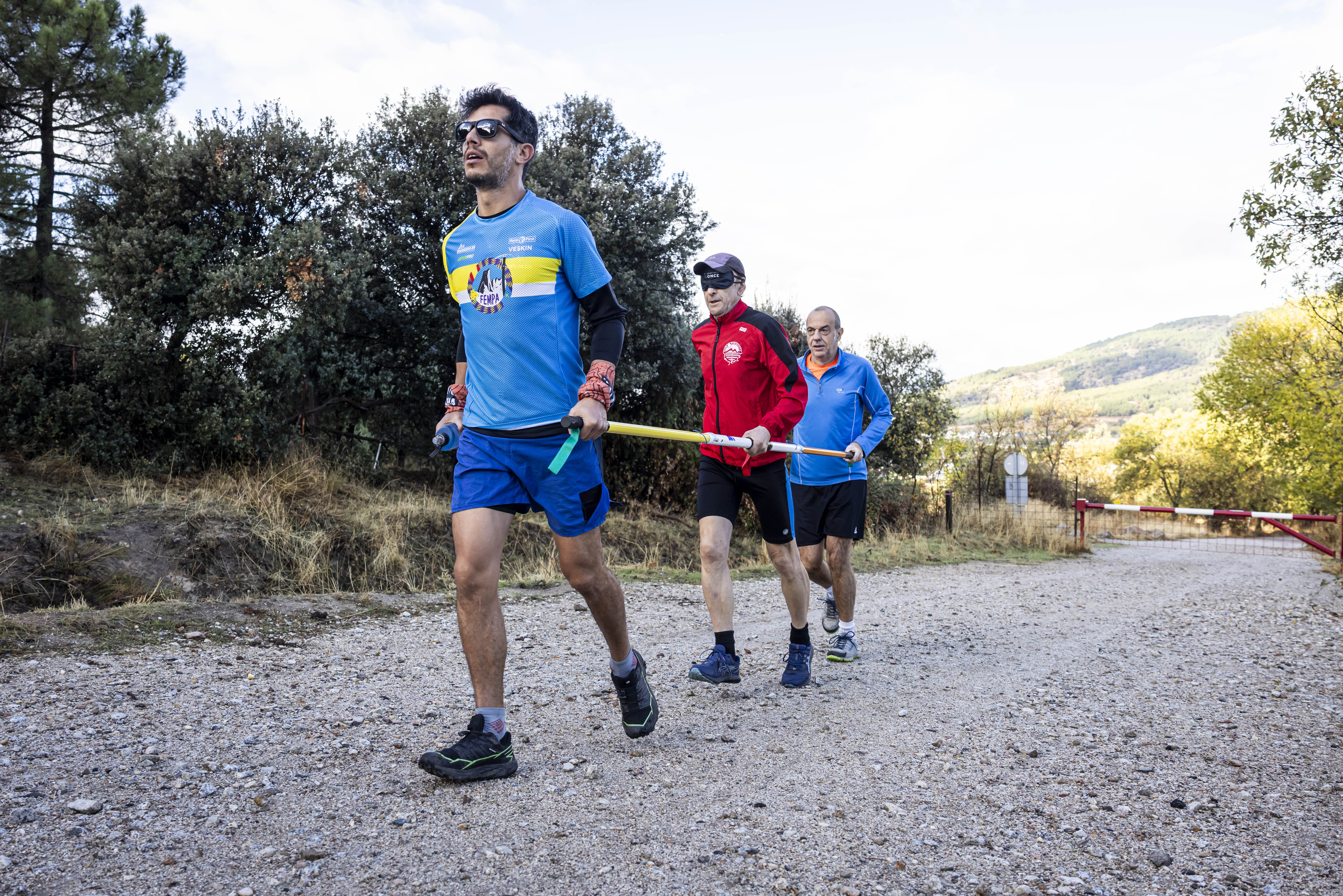 Participantes en el curso con la barra direccional con la que se realiza senderismo por montaña, con la persona ciega en el centro y el guía en primer lugar