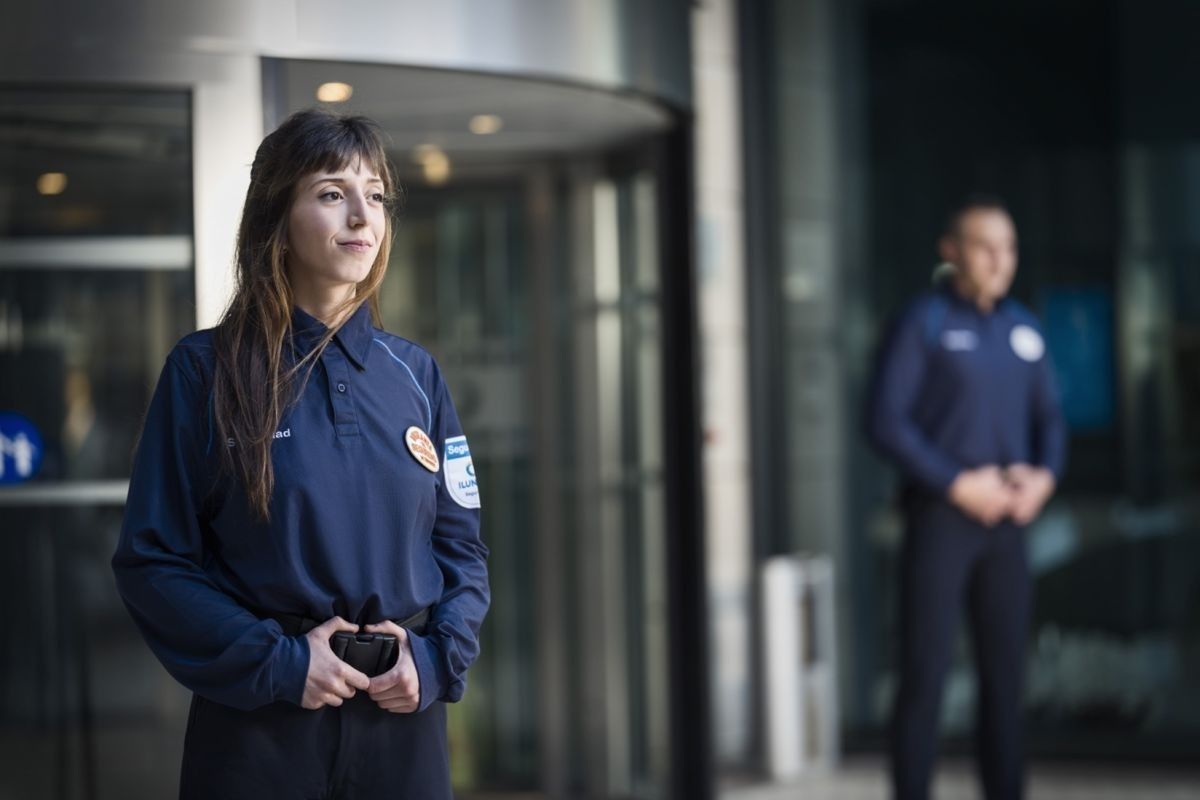 Dos vigilantes de ILUNION Seguridad, una mujer y un hombre, custodian la entrada de un edificio