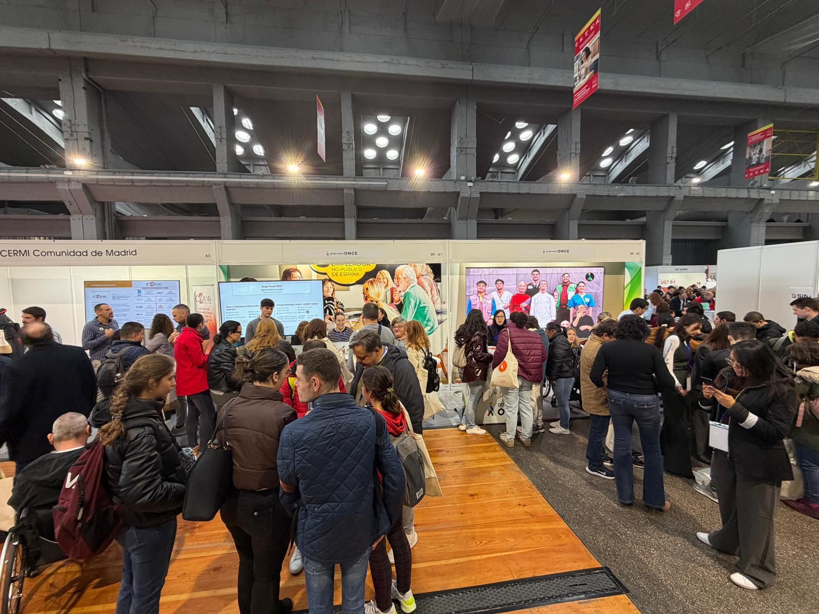 Stand del Grupo Social ONCE visto de frente, cartelería y pantallas, mucha gente delante