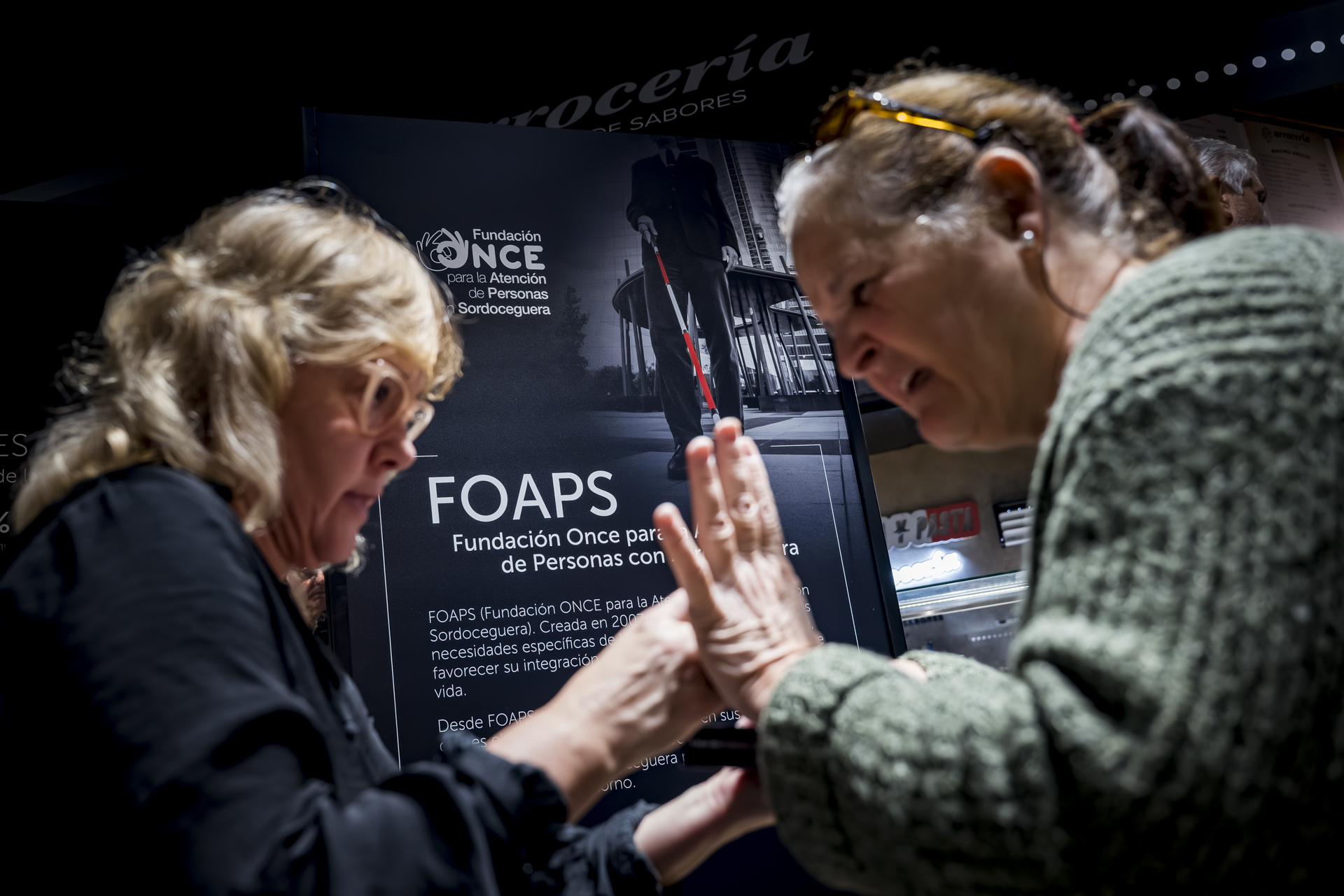 Una mujer sordociega junto a su mediadora en el acto de presentación del turrón accesible