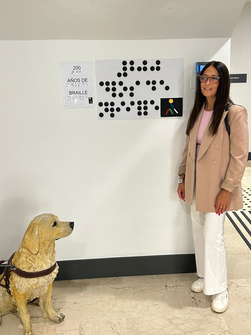 Susana Mangut junto a un cartel braille y la figura de perro guía