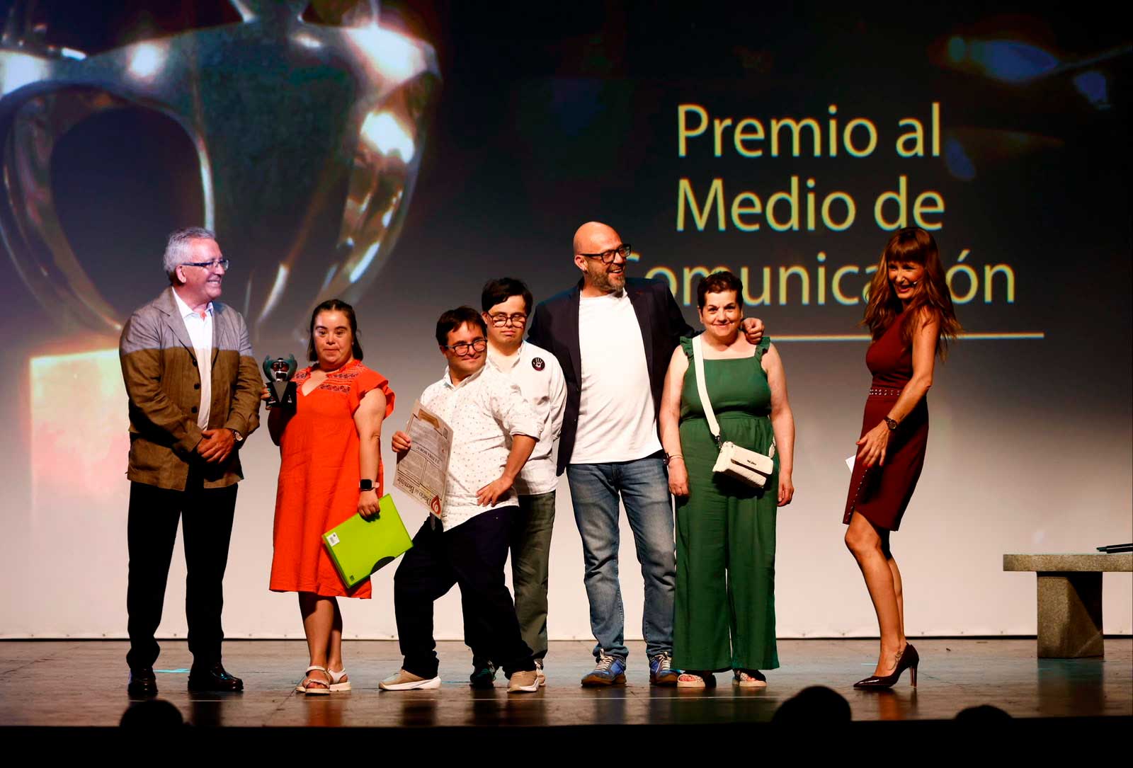 Grupo de personas sobre el escenario durante la entrega de un Premio Solidario. Una persona sostiene el galardón y otra un diploma, mientras detrás se proyecta el texto "Premio al Medio de Comunicación".
