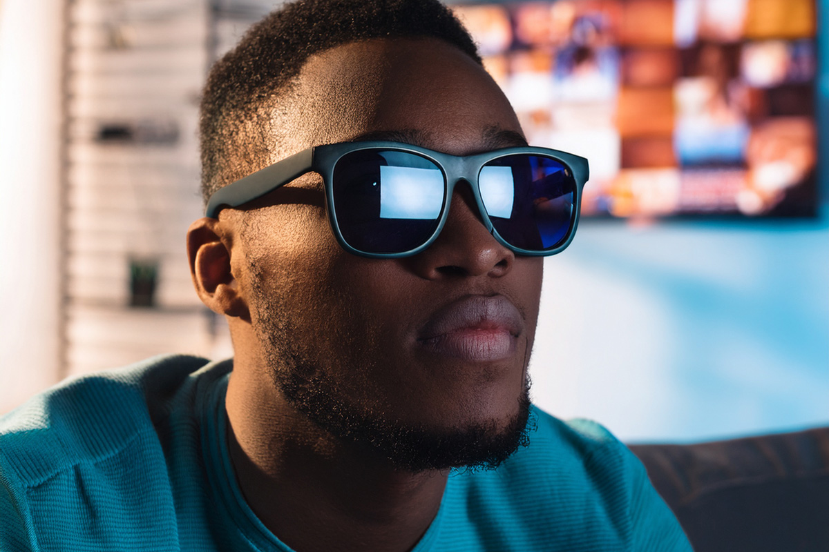 Una chico ciego con gafas de sol viendo la televisión, que se refleja en sus gafas.png